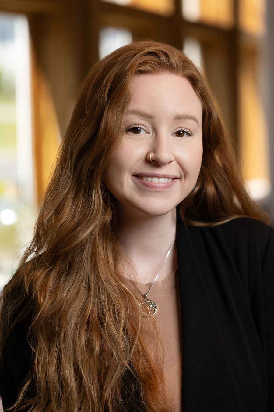 A woman with long red hair is wearing a black jacket and a necklace.