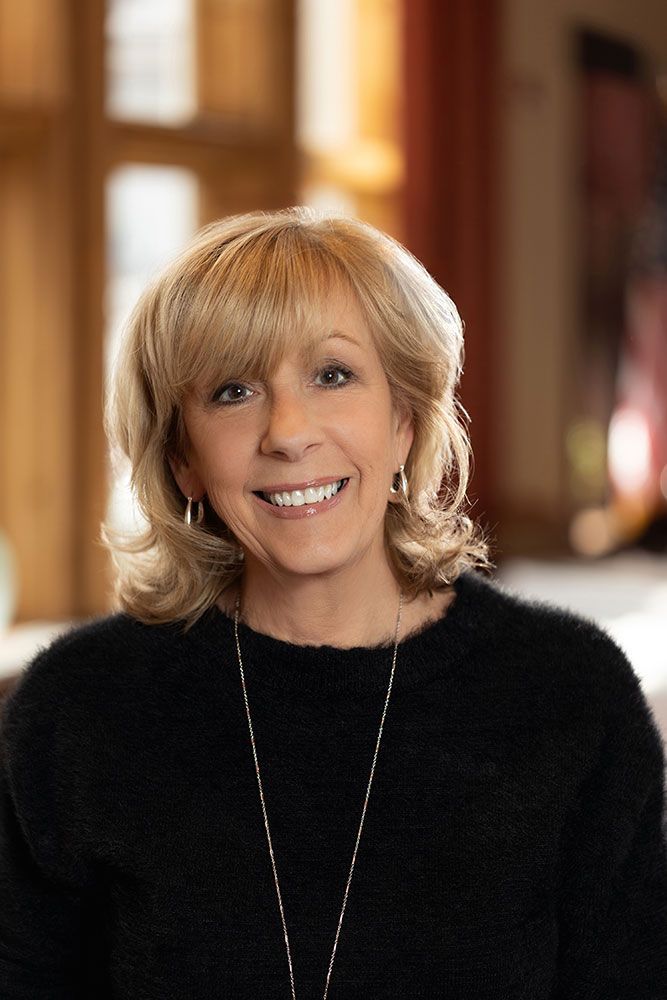 A woman wearing a black sweater and a necklace is smiling for the camera.