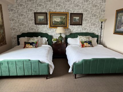 A hotel room with two queen beds and a lamp.
