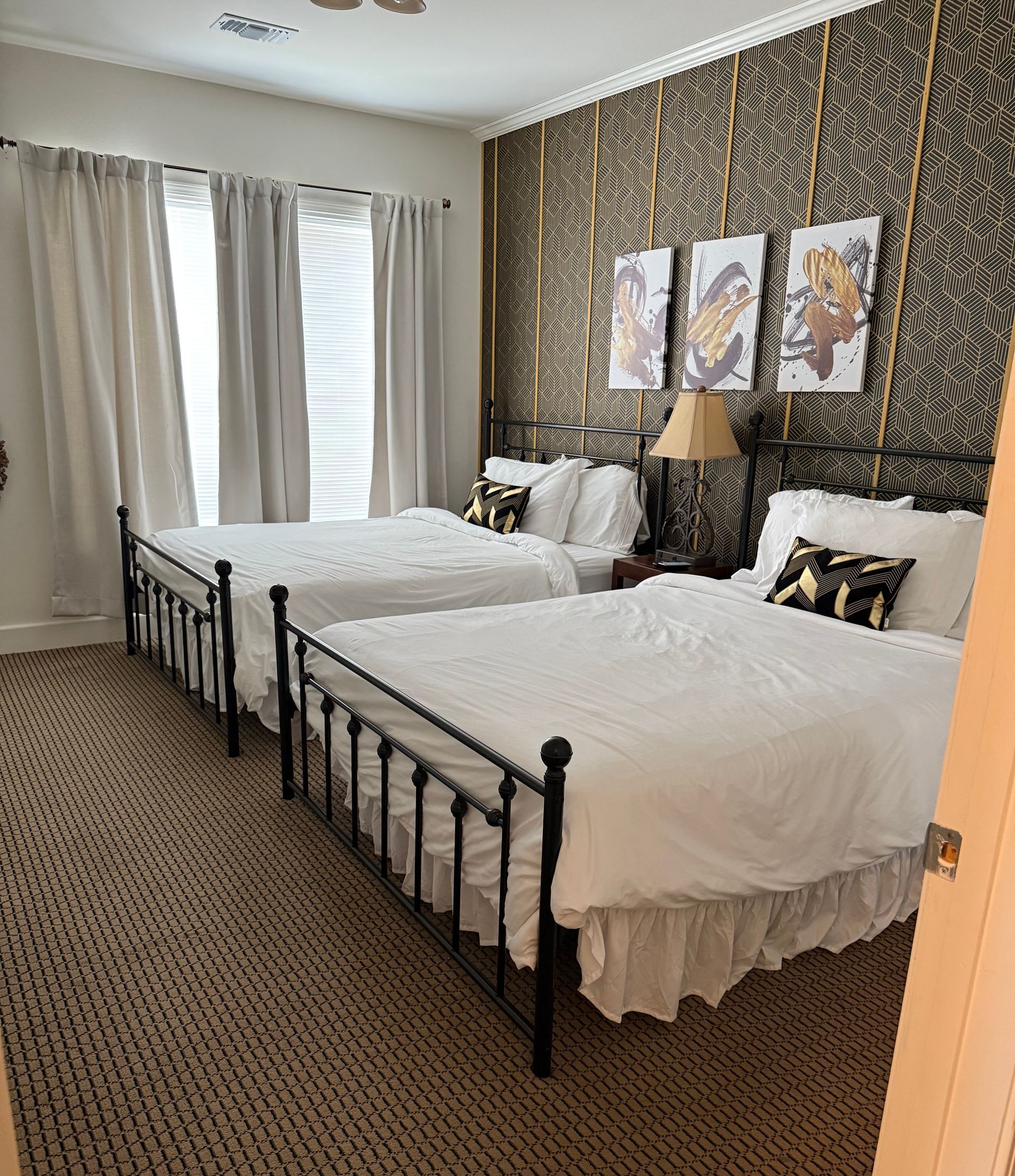 A bedroom with two queen beds , a lamp , and a window.