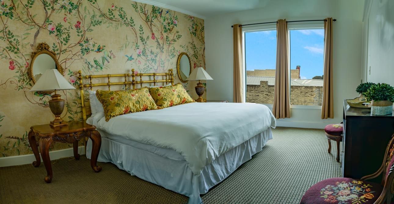 A bedroom with a king size bed , two lamps , a chair and a large window.