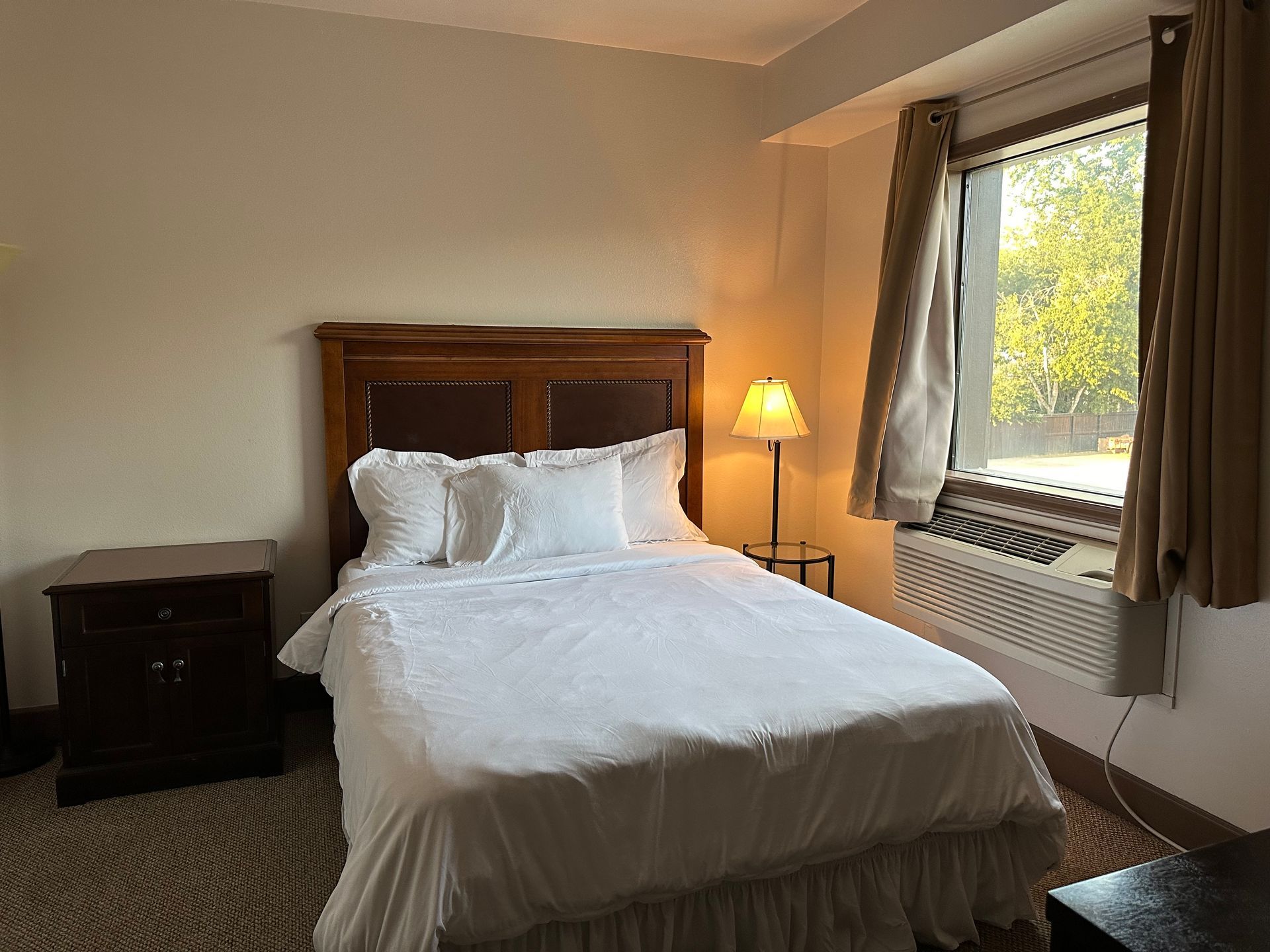 A bedroom with a bed , nightstand , lamp and window