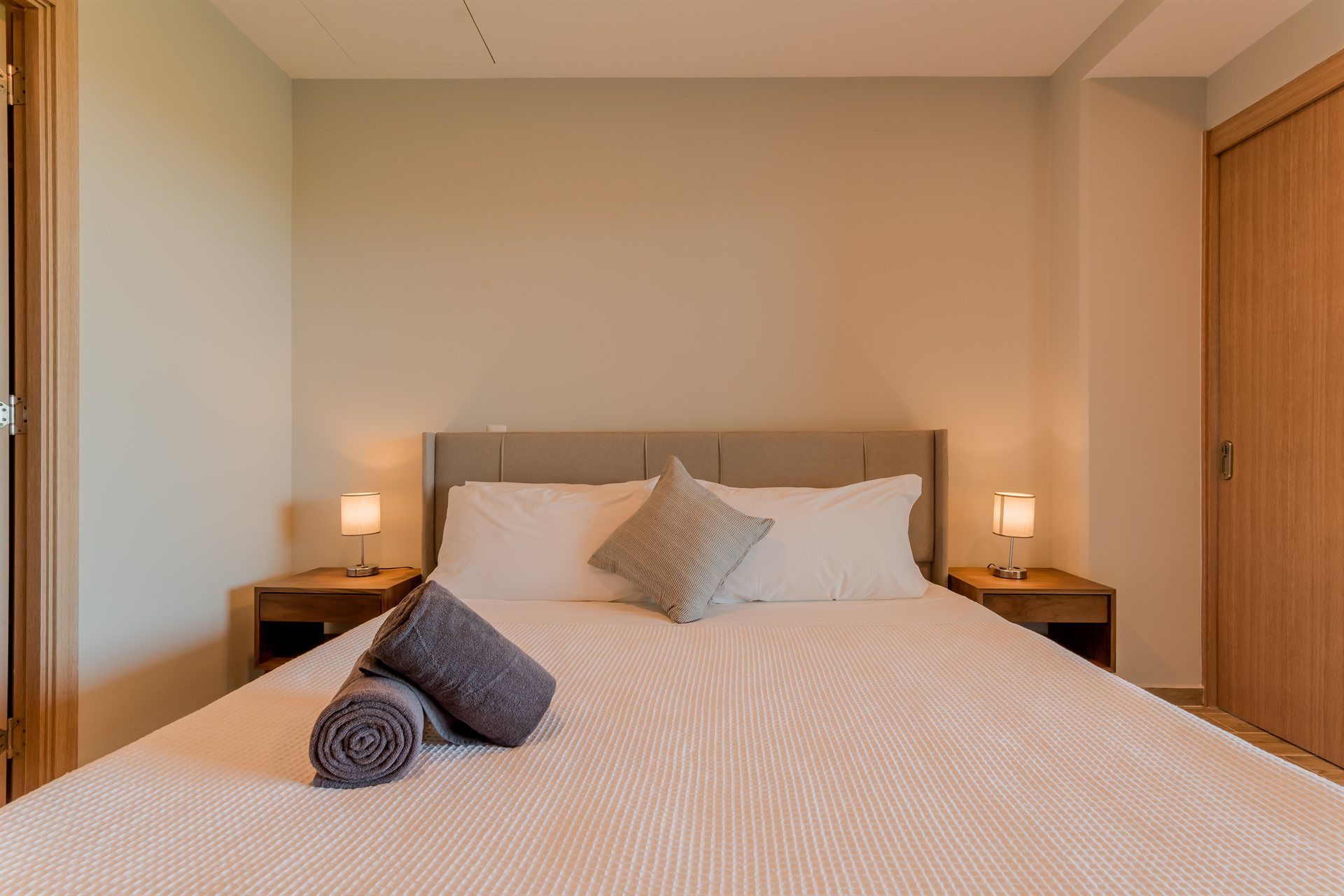 Un dormitorio con una cama, dos mesitas de noche, dos lámparas y dos toallas sobre la cama.