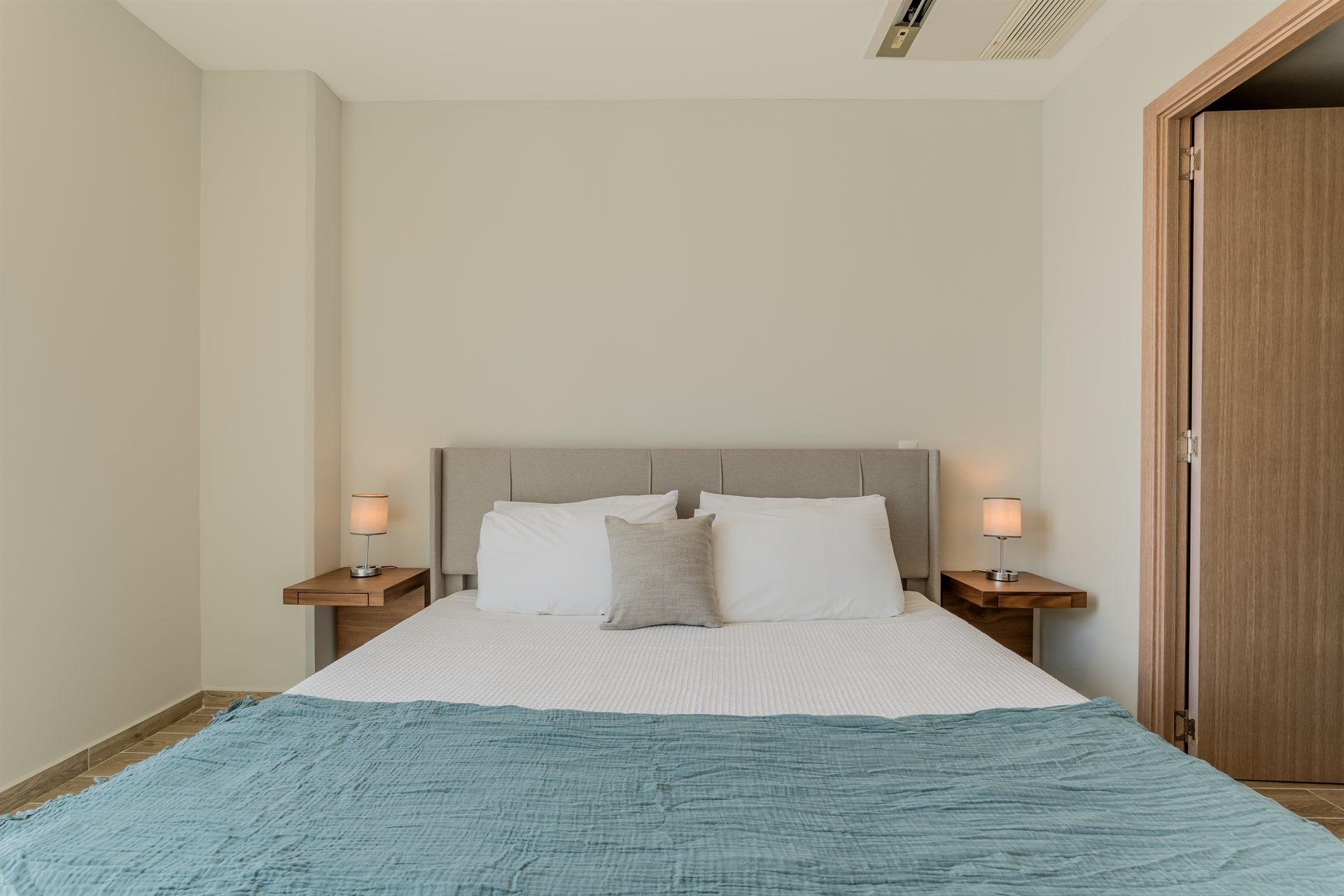 Un dormitorio con una cama, dos mesitas de noche, dos lámparas y una puerta.