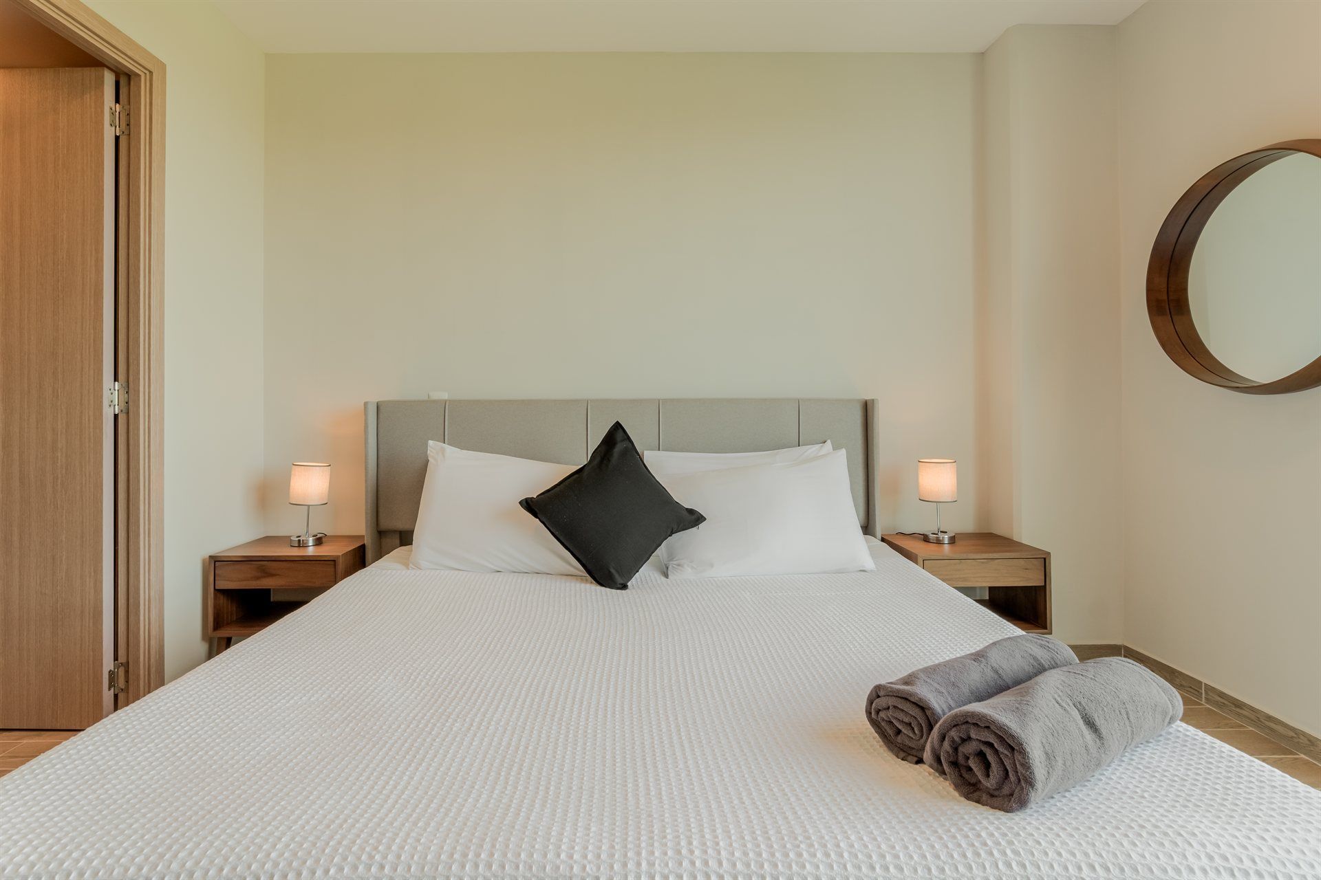 Un dormitorio con una cama, dos mesitas de noche, un espejo y dos toallas sobre la cama.