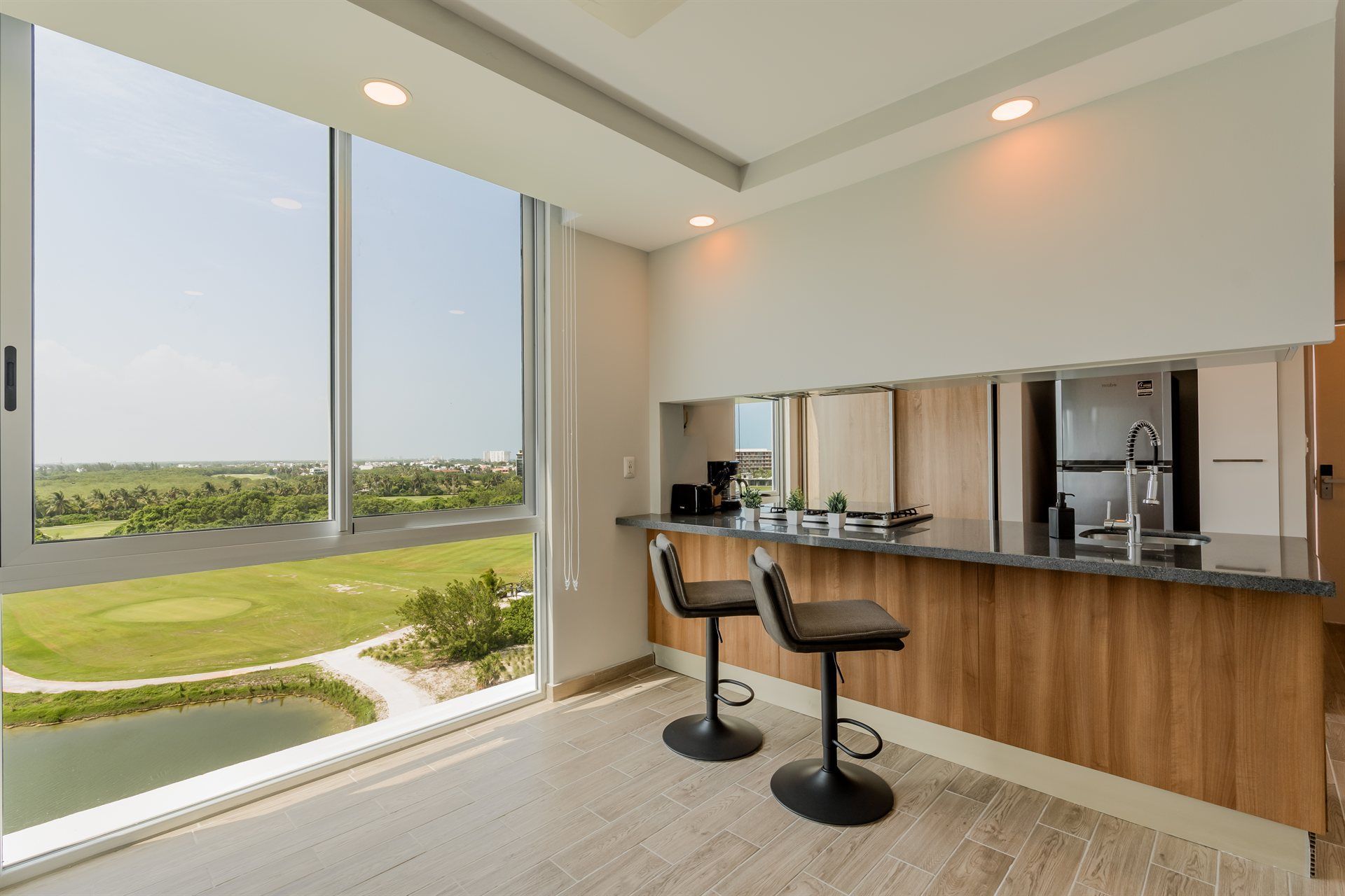 Una cocina con dos taburetes de bar y un gran ventanal con vista a un campo de golf.