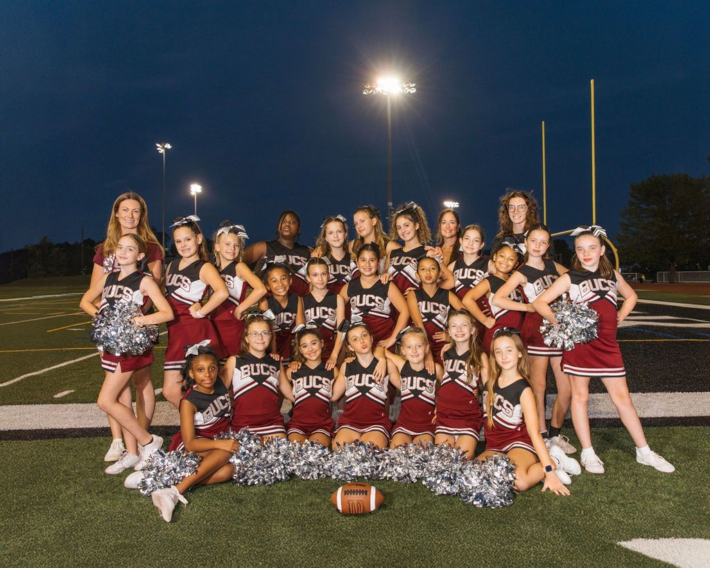 Cheerleader in red uniform performs a backbend on a green and red football field.