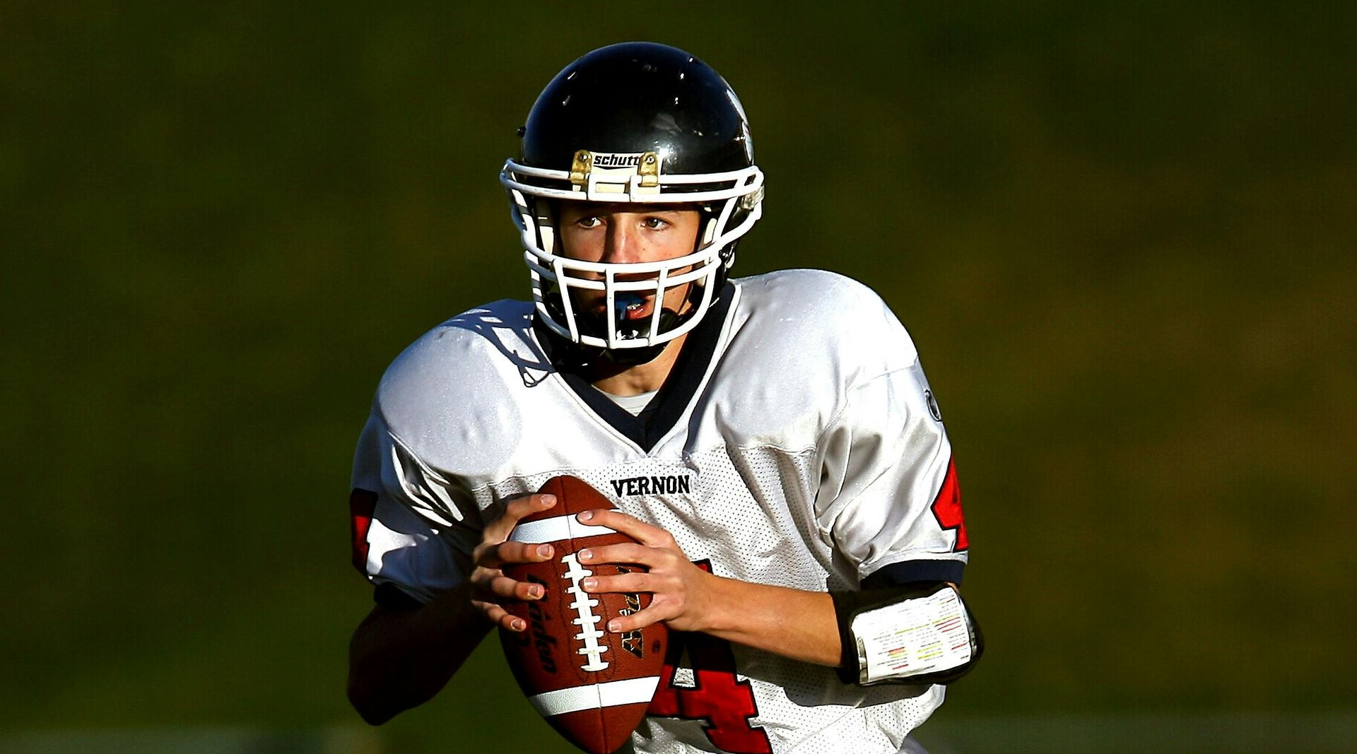 Football player in silver uniform runs with ball on a green field.