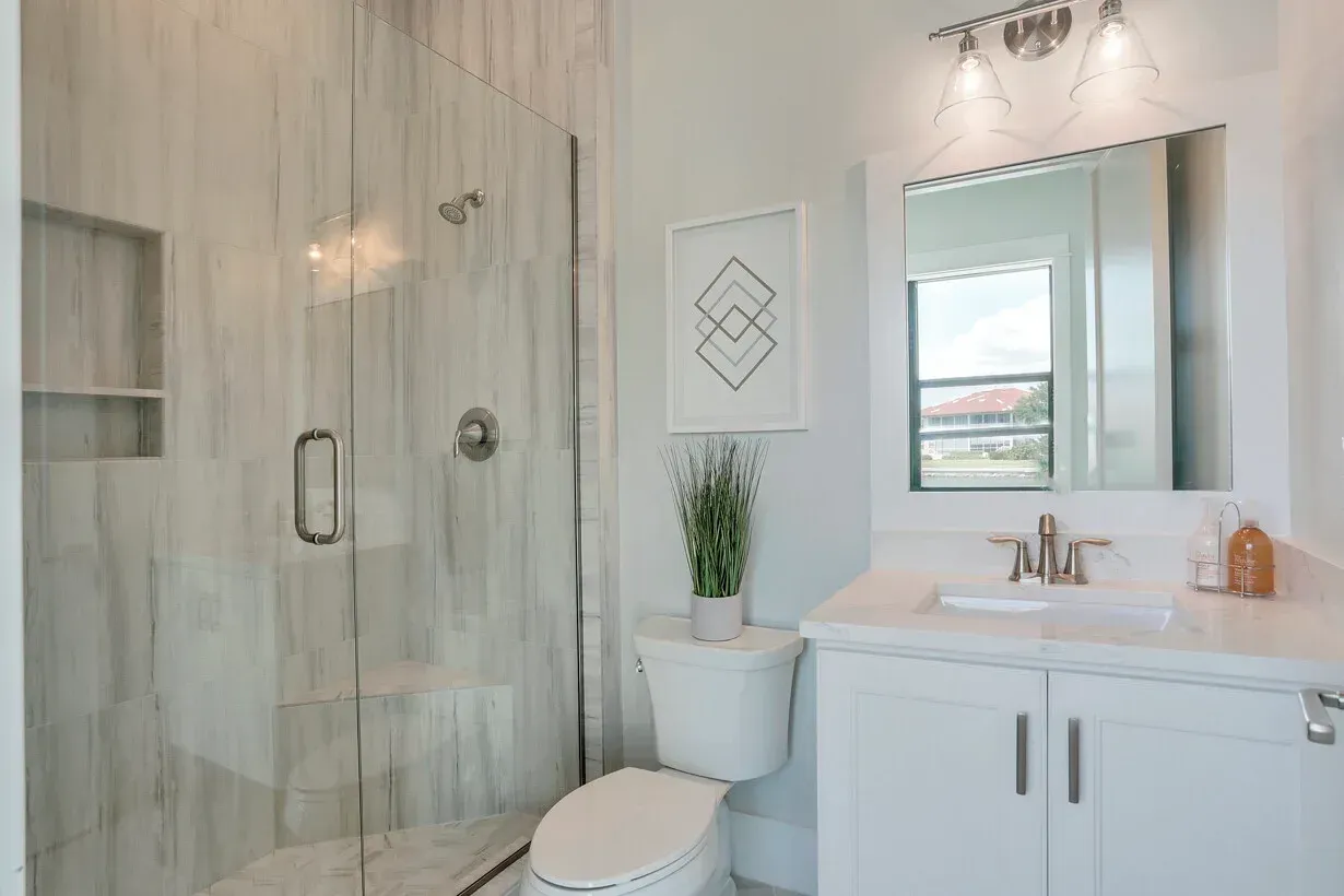 Bright bathroom with glass shower, white vanity, mirror, and toilet.