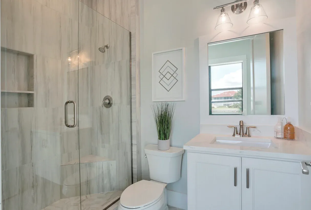 Bright modern bathroom with glass shower, white vanity, mirror, and toilet
