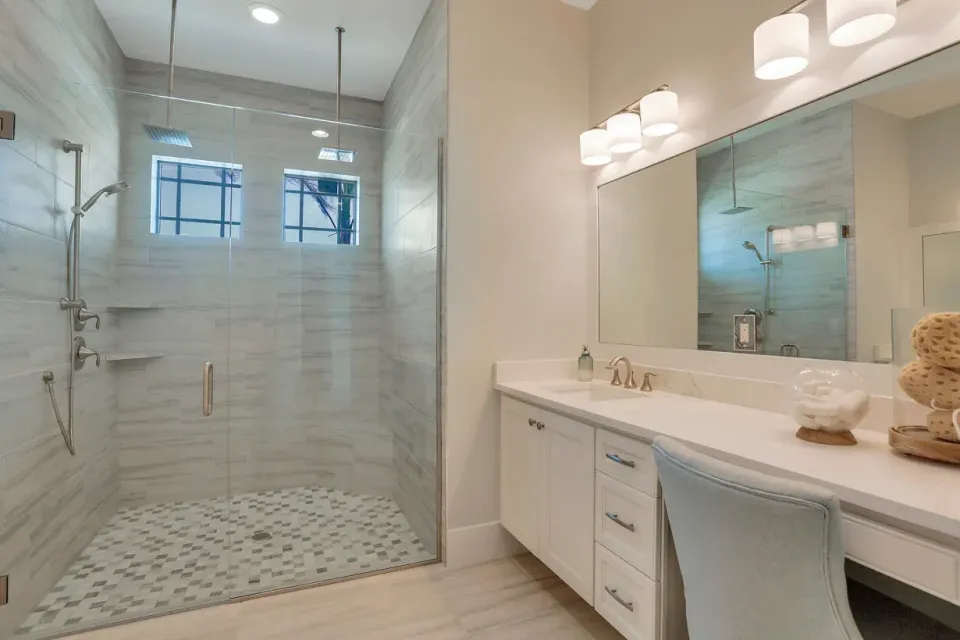 Bright white bathroom with glass shower, double vanity, and large mirror with pendant lights
