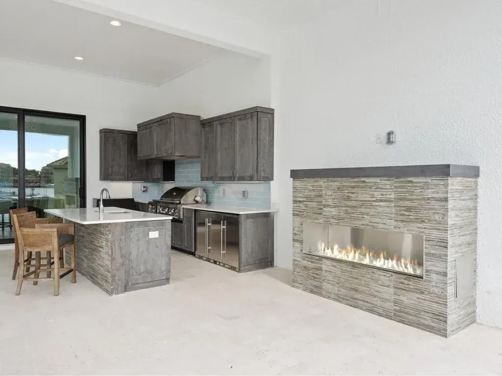 Modern open-concept kitchen and living area with gray cabinets and a stone fireplace.