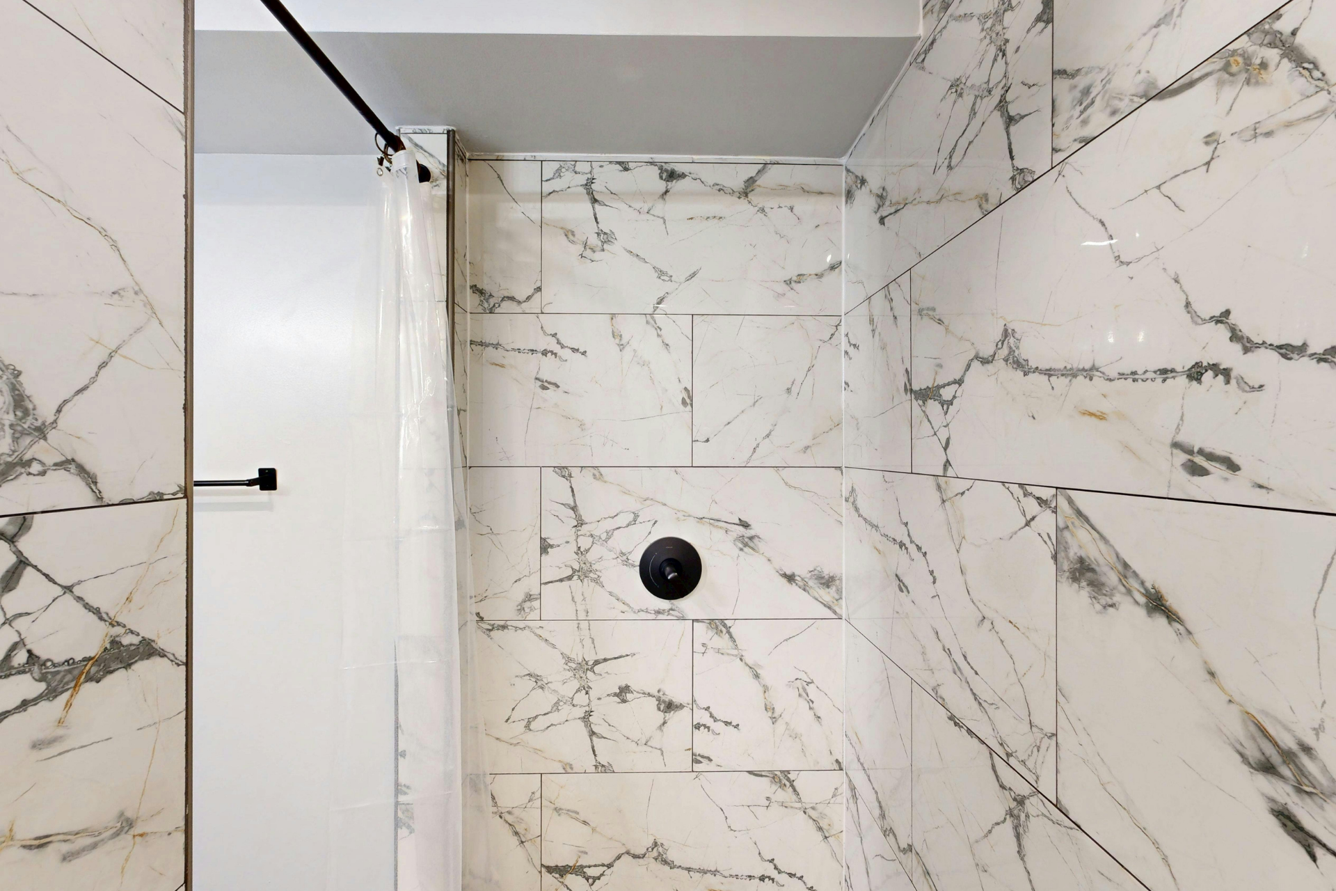 Marble-tiled shower with glass door and black shower fixture