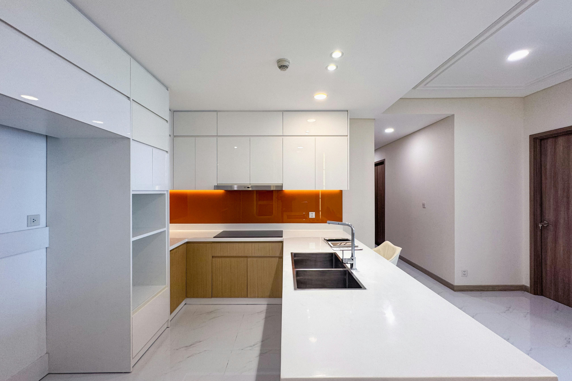 Modern white kitchen with an island, built-in appliances, wood cabinets, and orange under-cabinet lighting