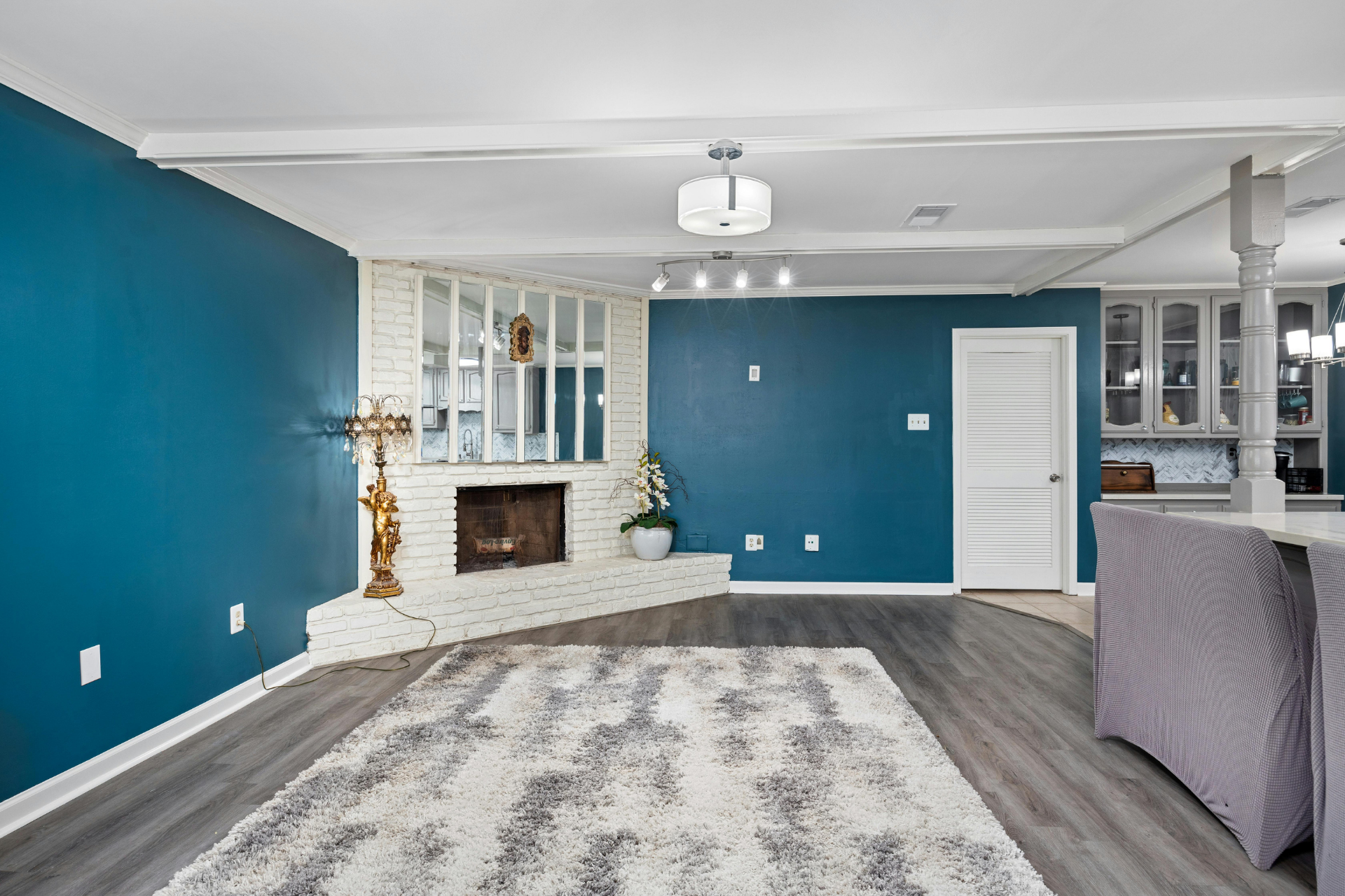 Empty living room with teal walls, white fireplace, gray rug, and hardwood floors