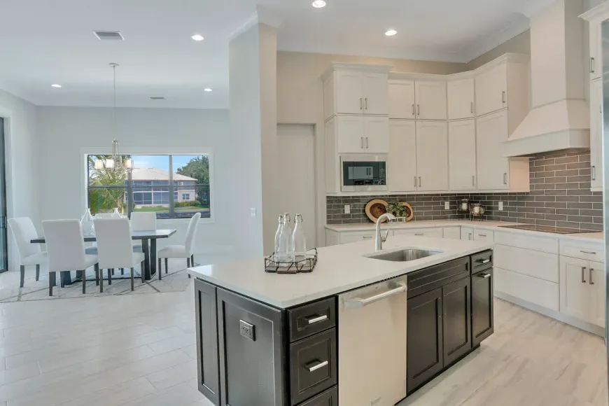 Bright modern kitchen with white cabinets, dark island, and open dining area by large windows