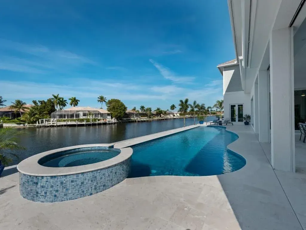 Luxury backyard pool and hot tub beside a waterfront patio under a clear blue sky