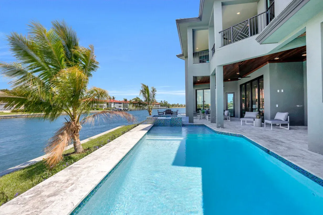 Modern waterfront villa with a turquoise pool, palm tree, and ocean view