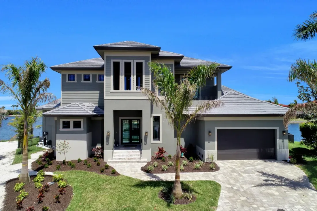 Modern two-story gray house with palm trees, front lawn, and a two-car garage under a blue sky