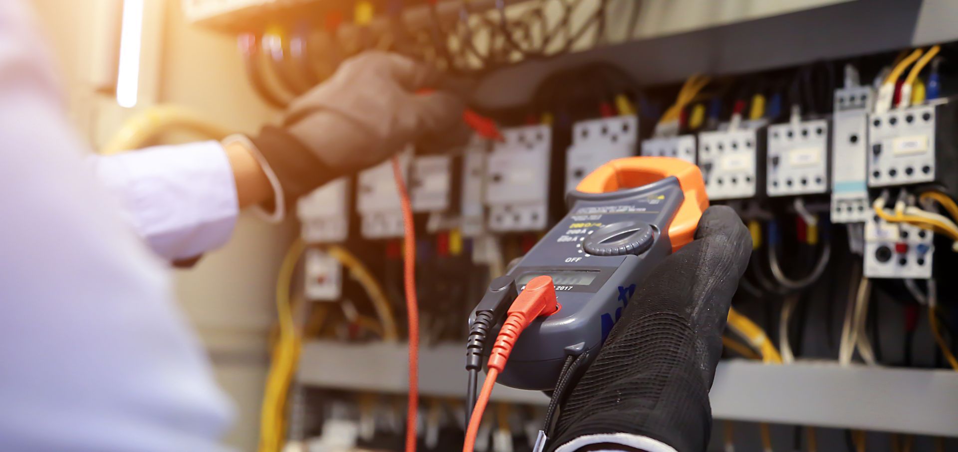 Technician using a multimeter to test electrical connections inside a control panel with wiring.