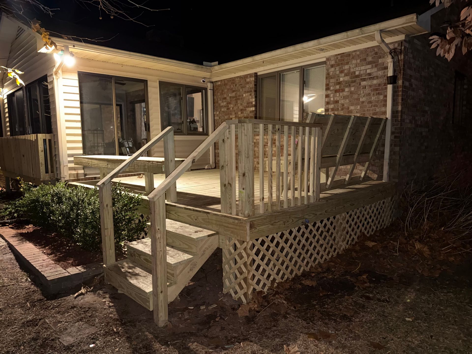 Wooden deck with steps leading up to a brick building at night; lights illuminate the deck.