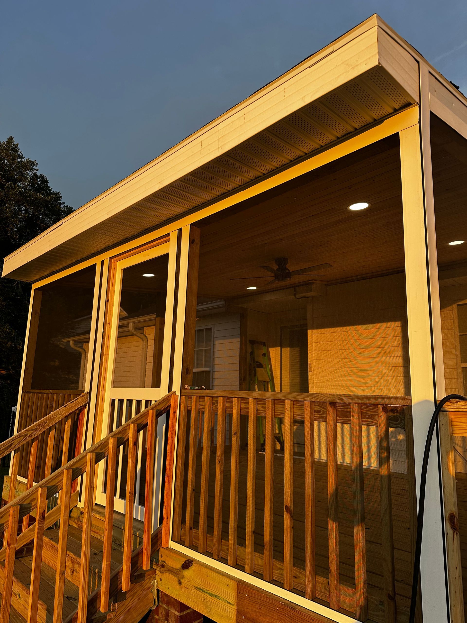 Screened-in porch with wood railings and trim, lights, and a ceiling fan, during dusk.