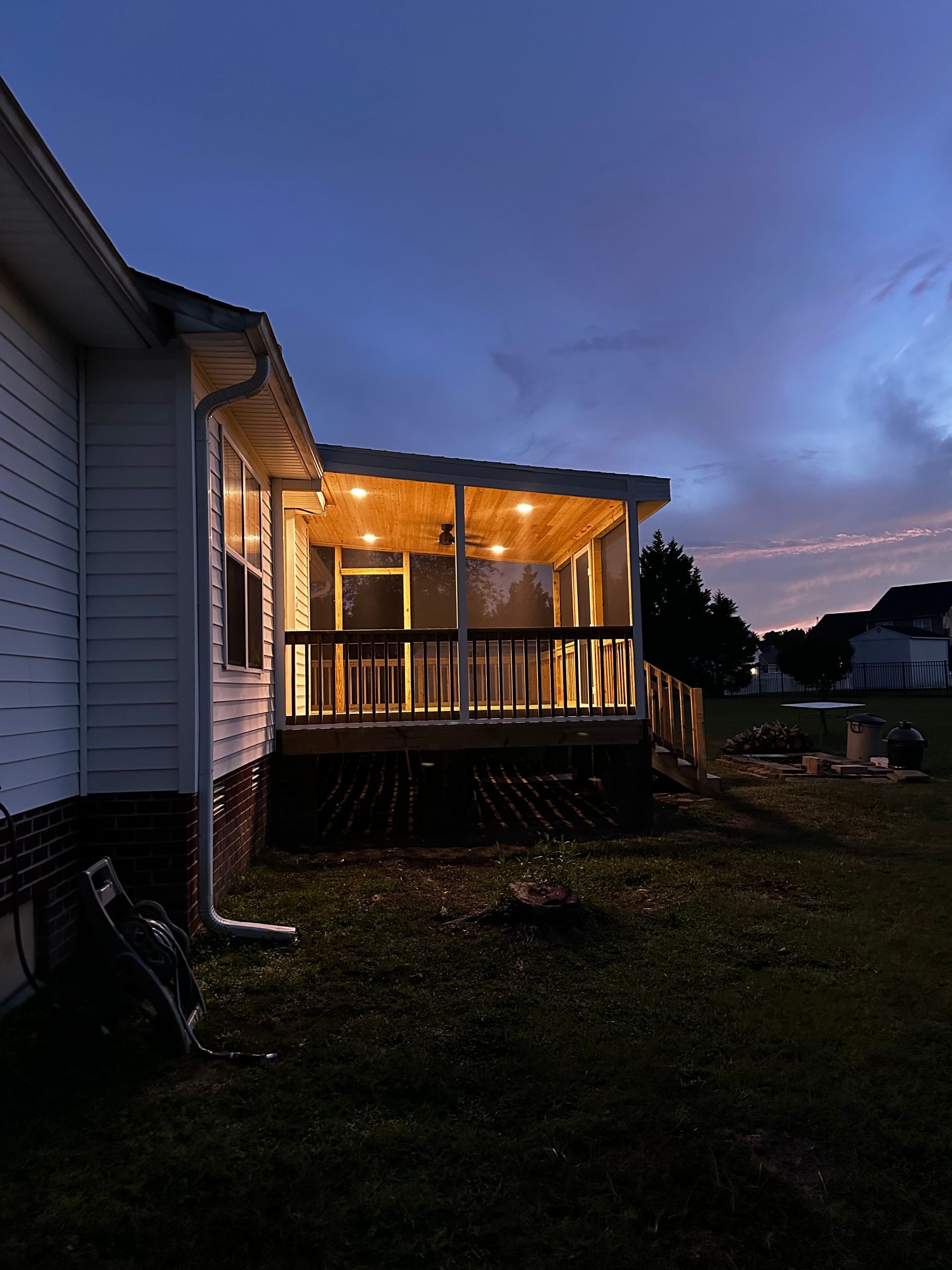 Lit-up porch attached to a house at dusk. Wooden deck with string lights. Overcast sky with hues of pink and blue.