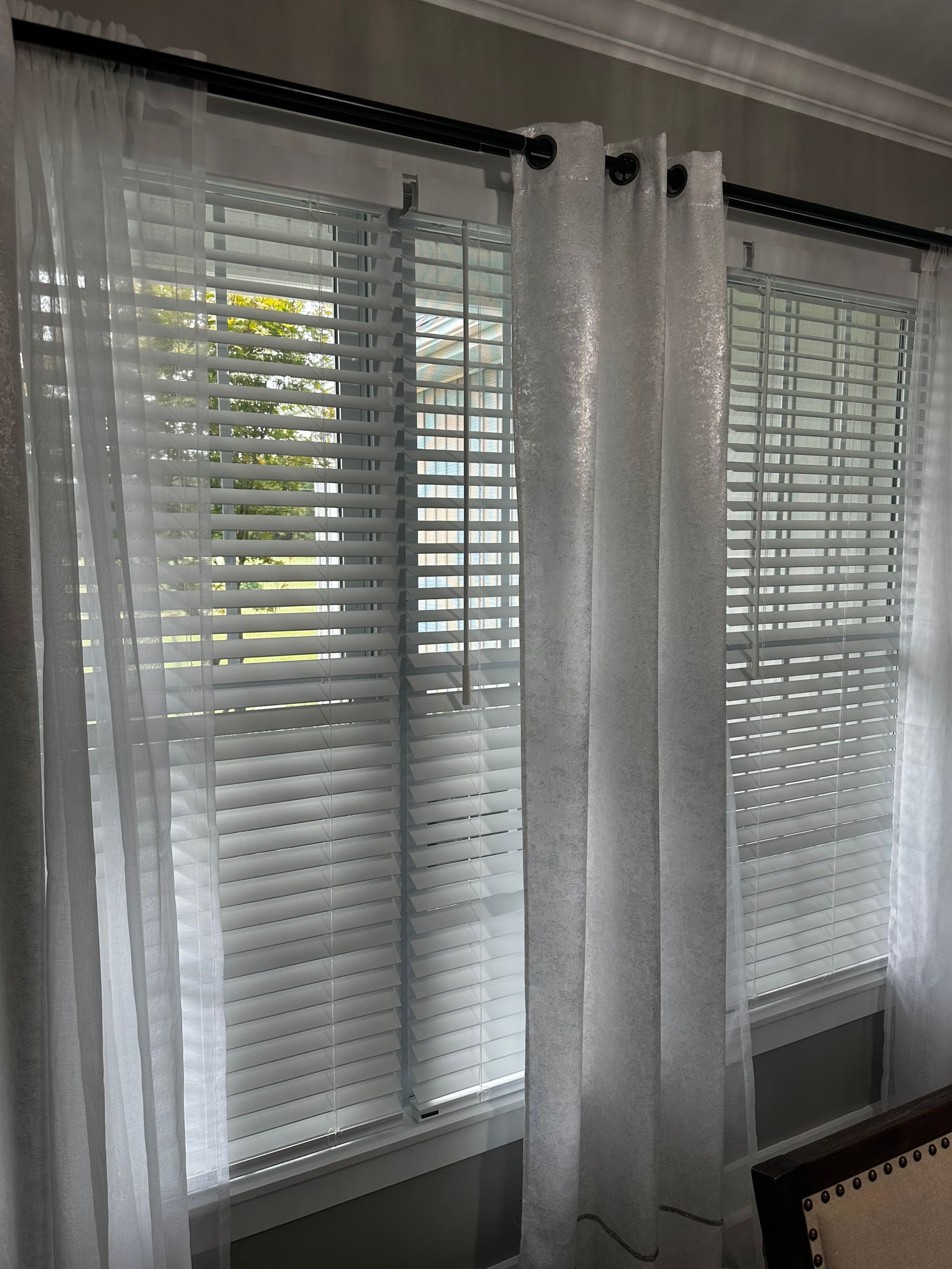 Sheer white curtains framing a window with closed blinds.