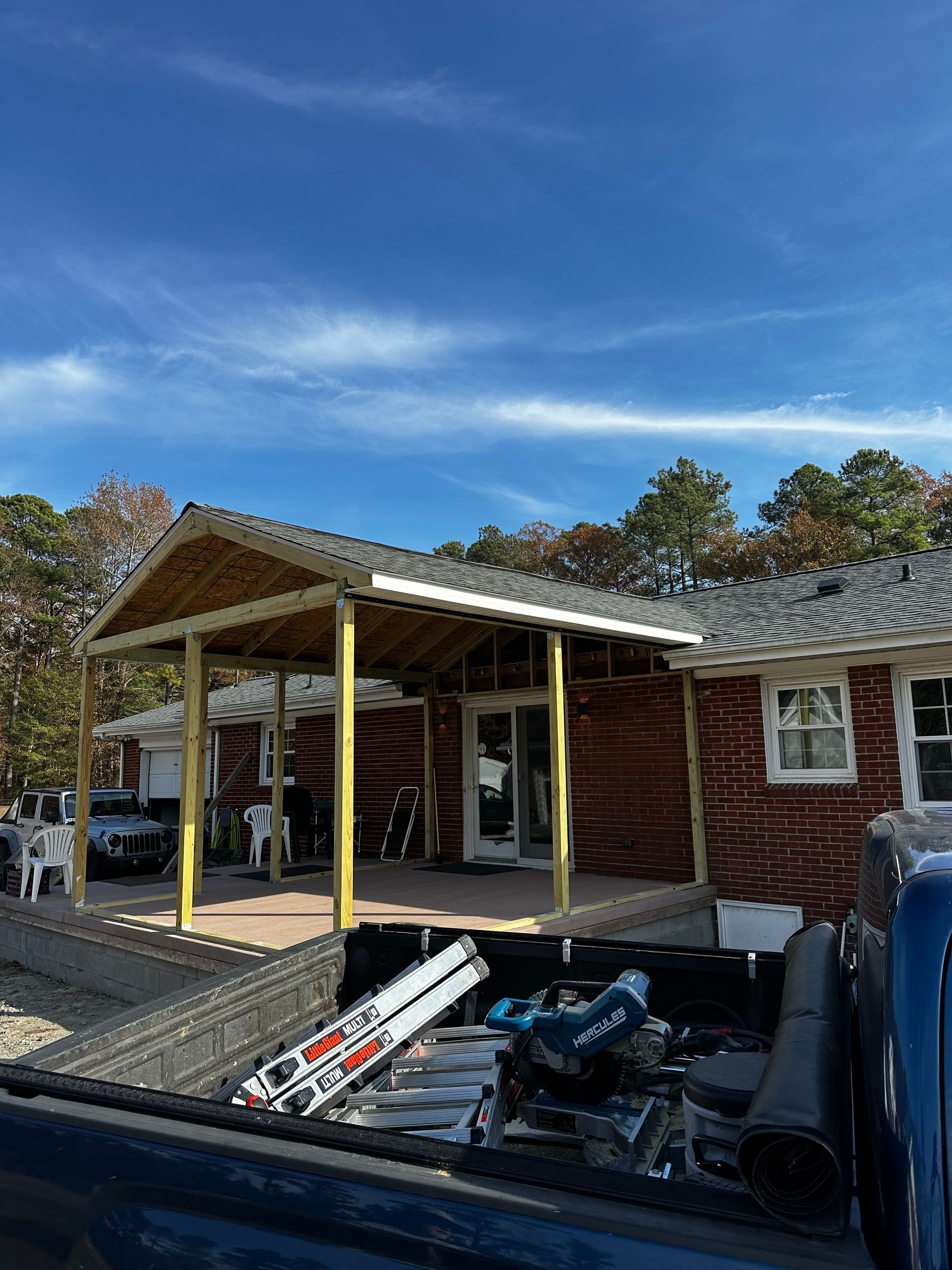 Newly constructed wooden porch extension on a red brick house under a blue sky.