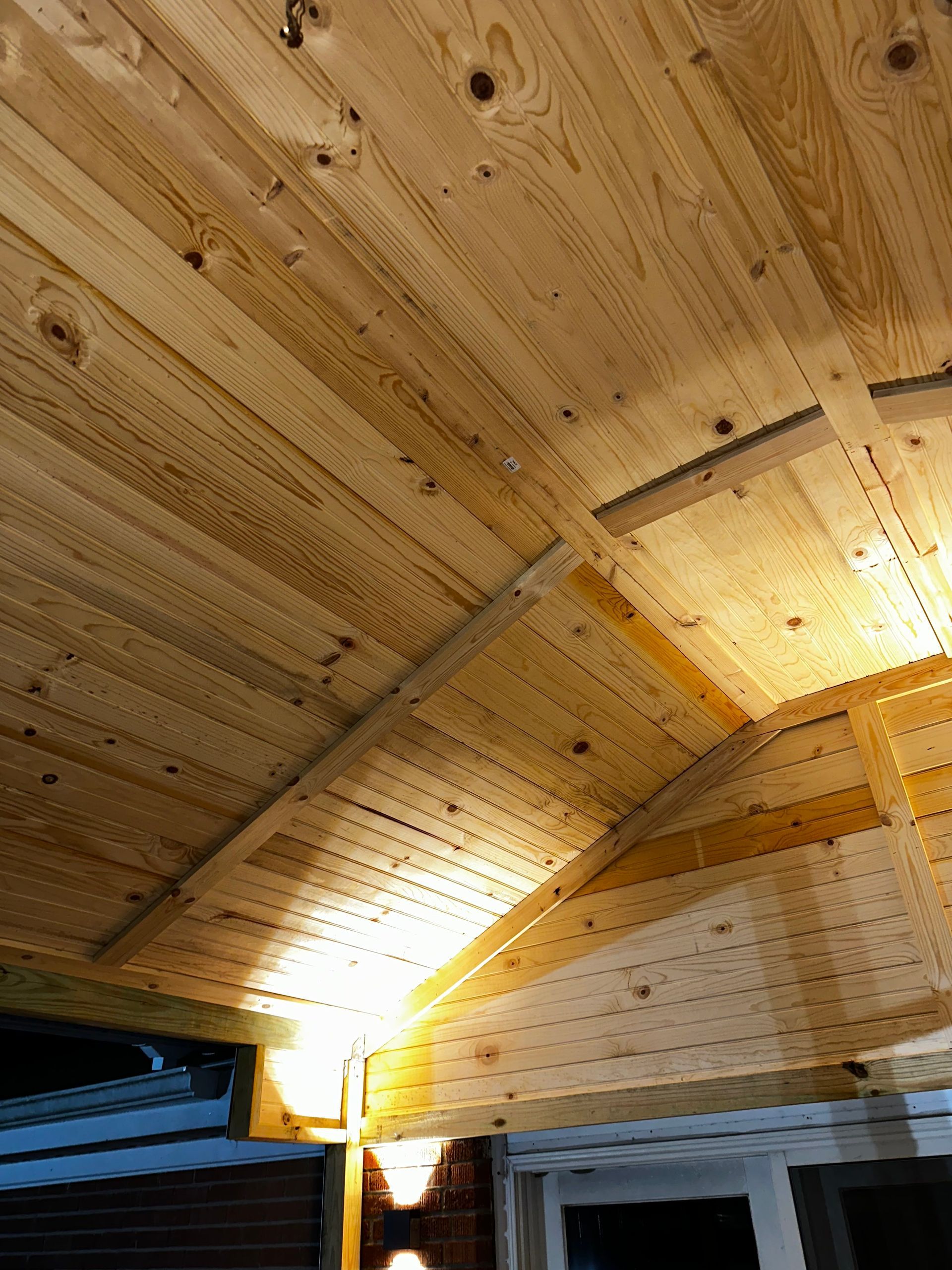 Wooden ceiling with beams and rafters, lit by warm light, likely an outdoor covered area.