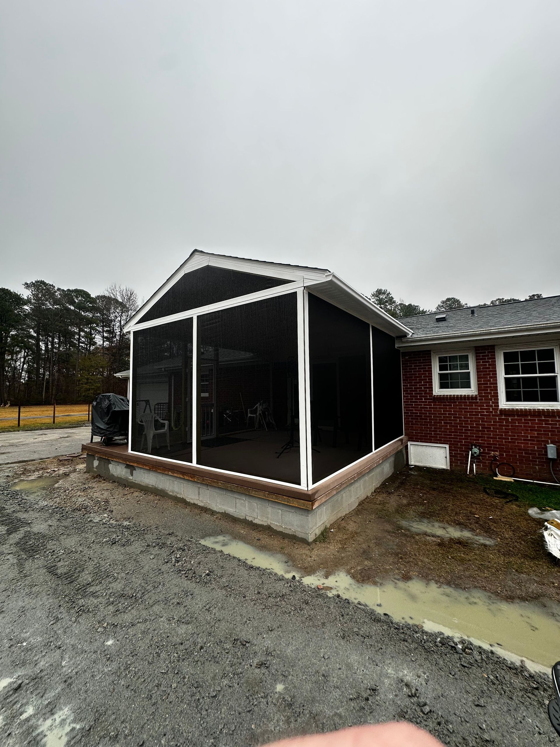 Screened-in porch addition with white framing, attached to a brick home on a cloudy day.