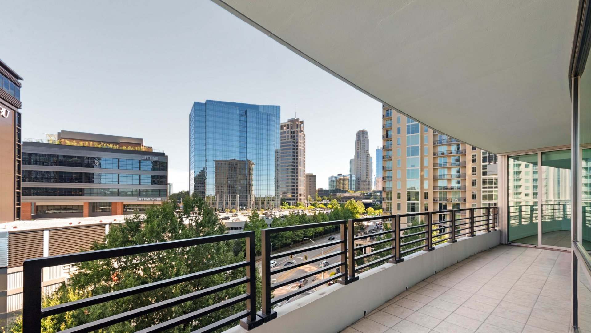View from a balcony overlooking a city skyline with modern glass buildings, blue sky.