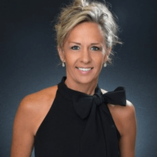 Woman with blonde hair in a black halter top, smiling. Against a dark background.