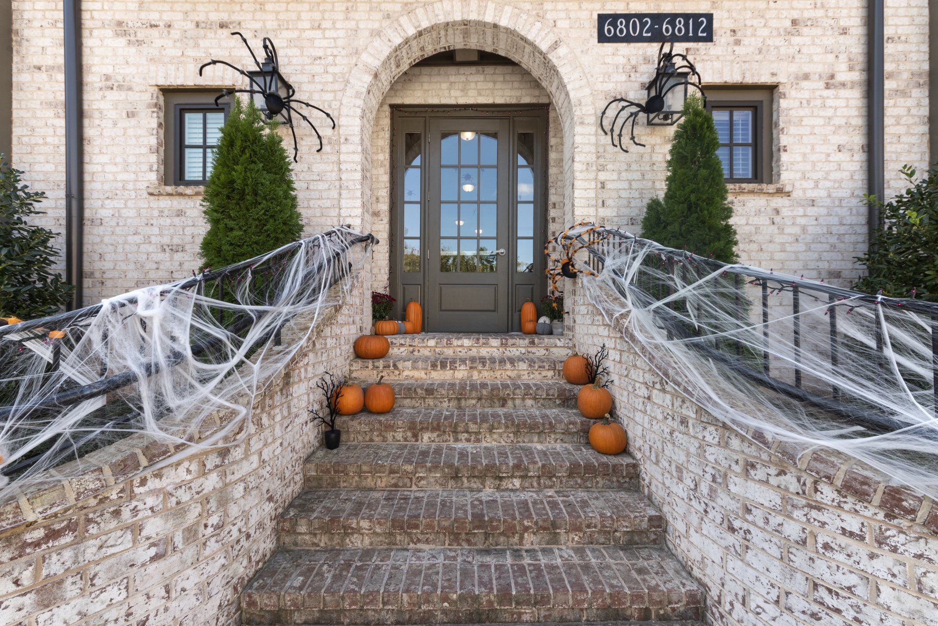 The front of a brick house decorated for halloween with pumpkins and spider webs.