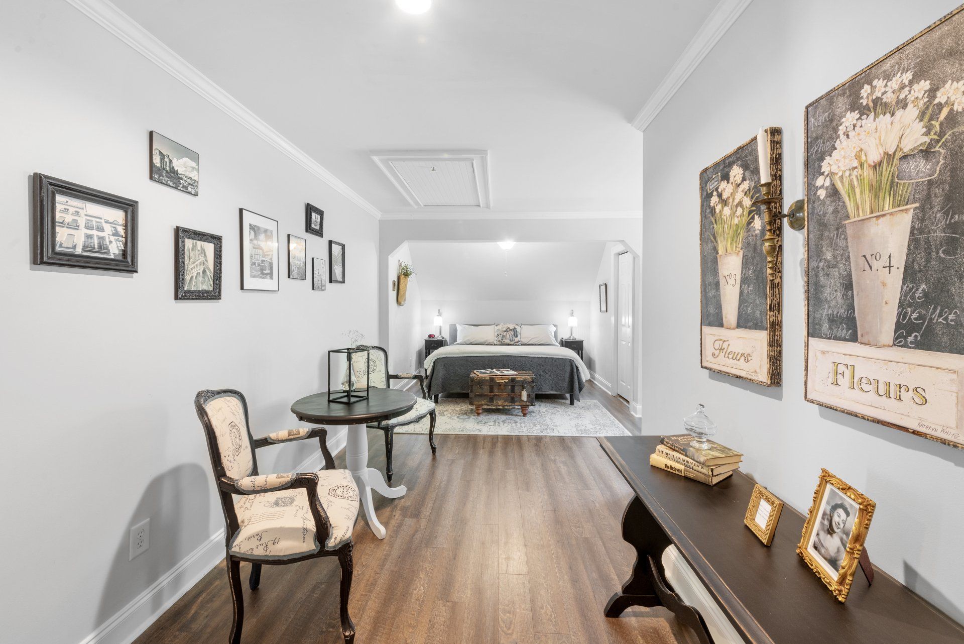 A hallway with a table , chairs , and pictures on the wall leading to a bedroom.