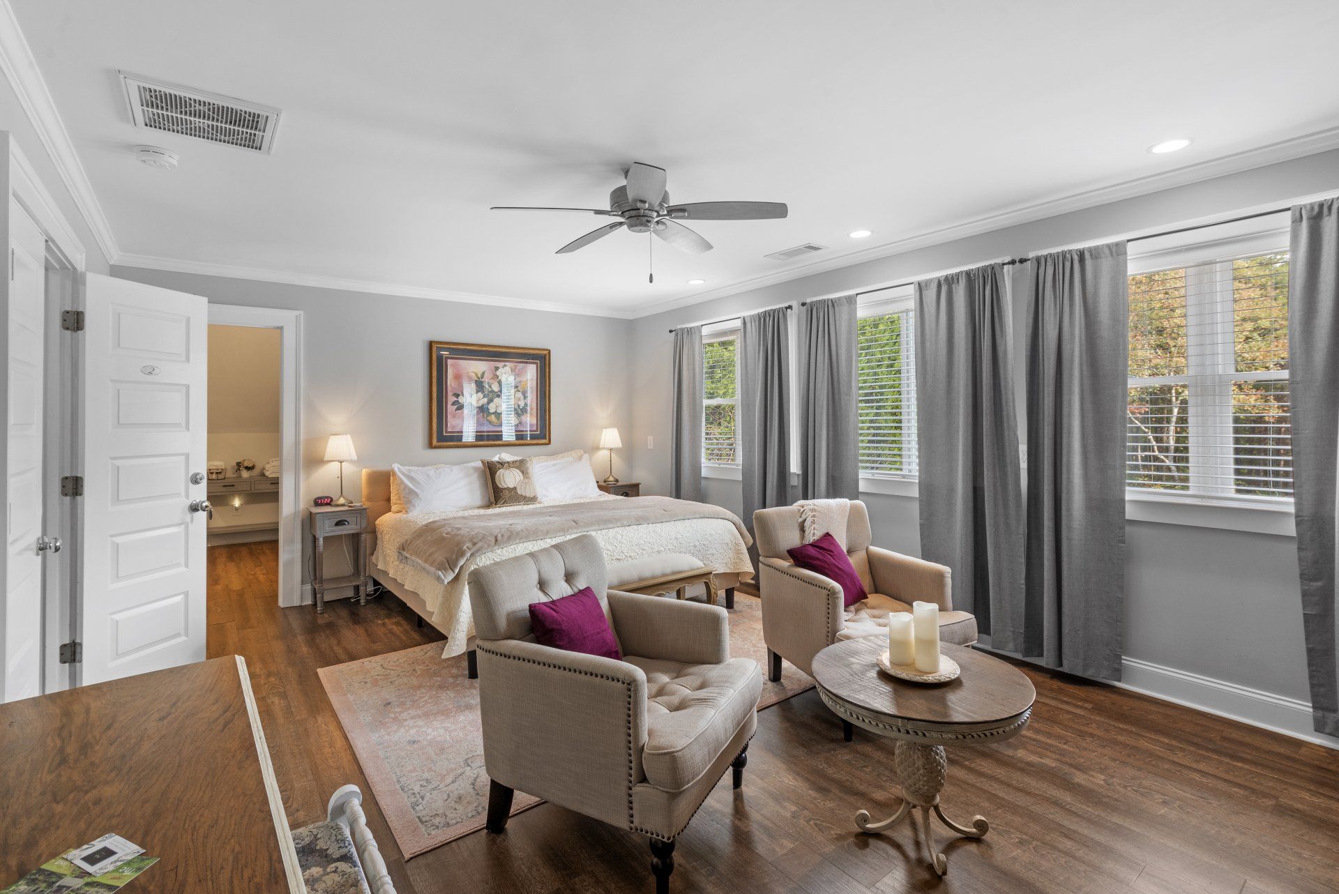 A large bedroom with a bed , chairs , a table and a ceiling fan.