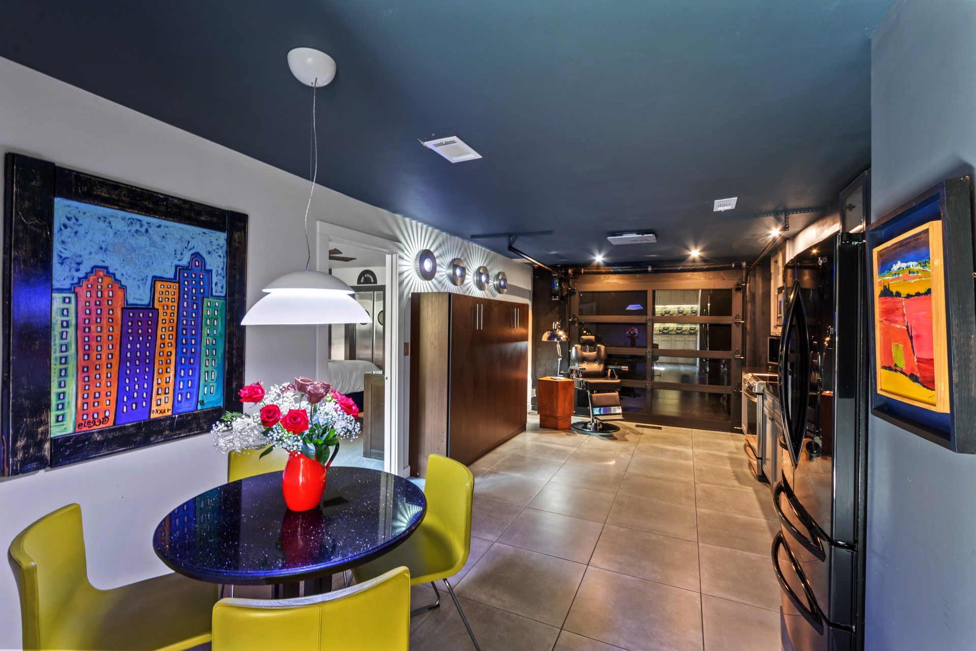 A dining room with a table and chairs and a painting on the wall.