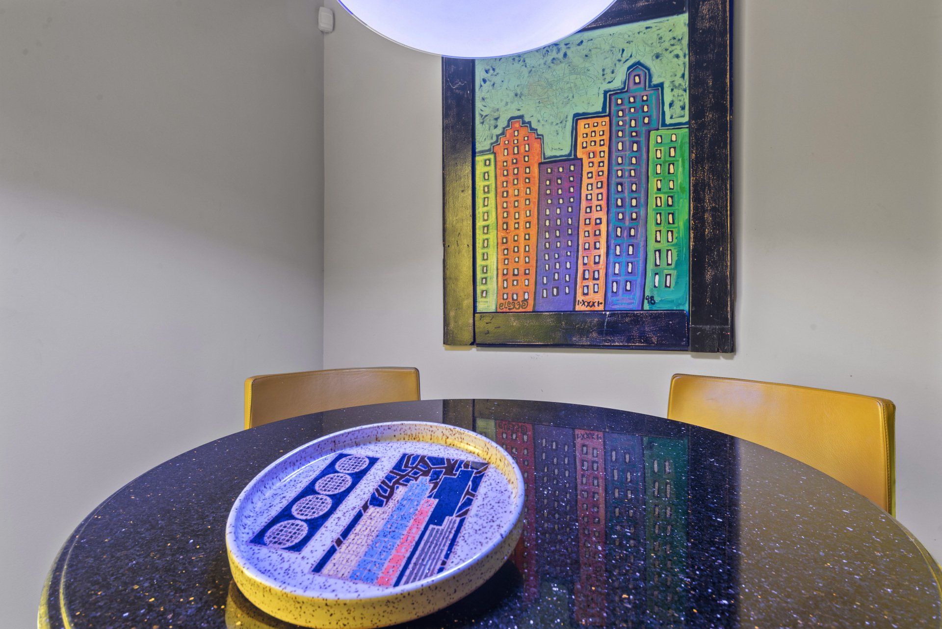 A dining room table with a plate on it and a painting on the wall.
