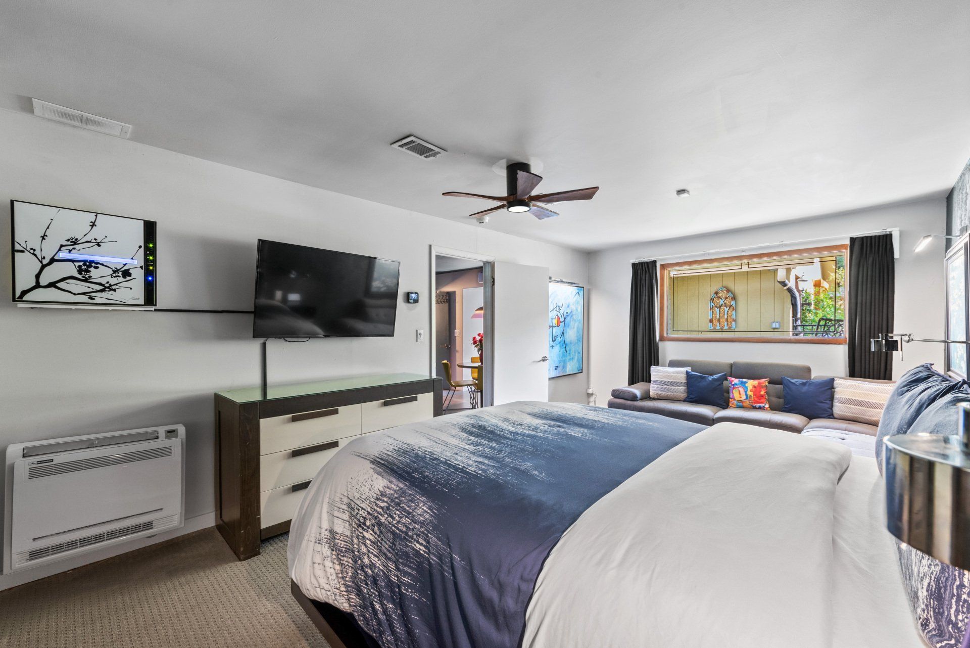 A bedroom with a king size bed , television , dresser and ceiling fan.