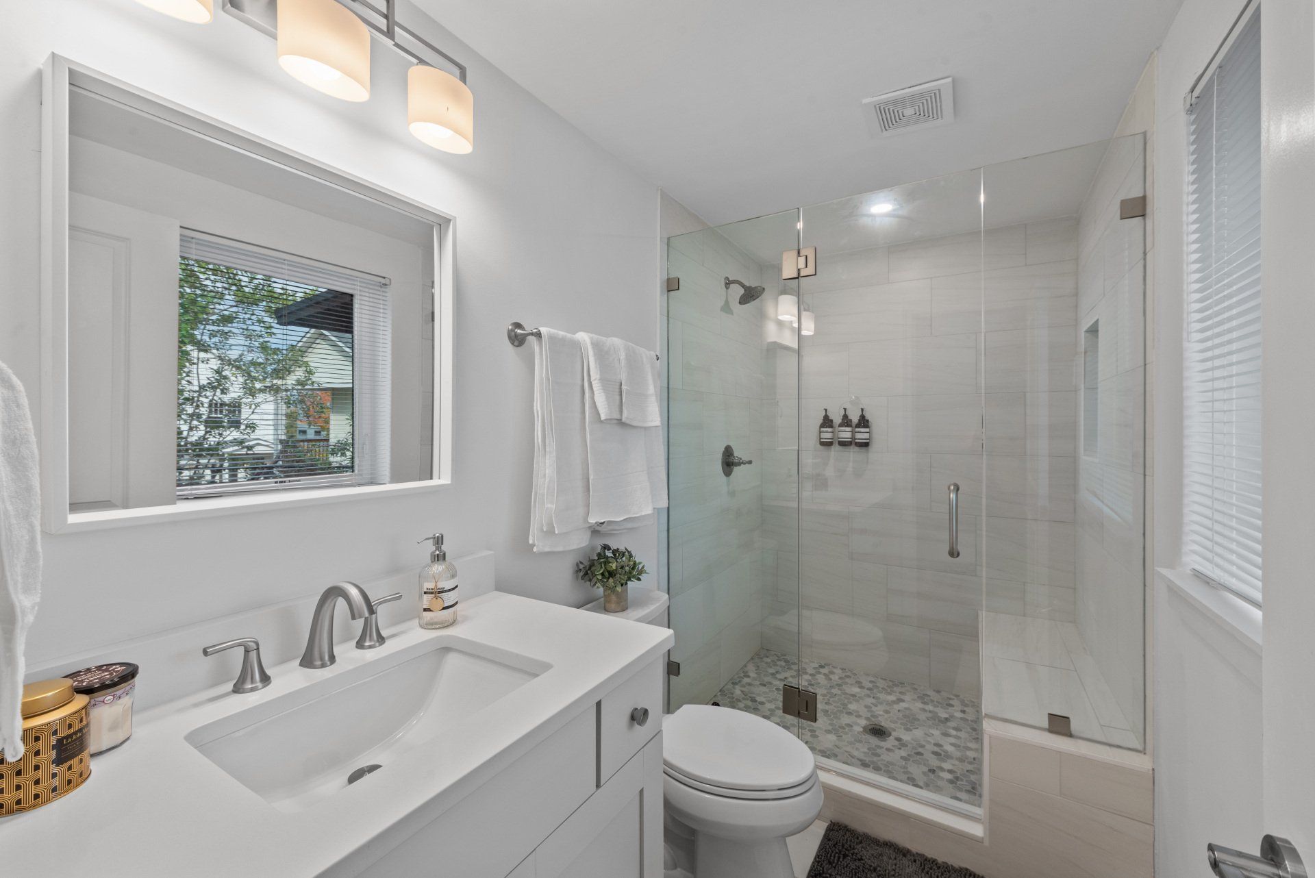 A bathroom with a sink , toilet , shower and window.