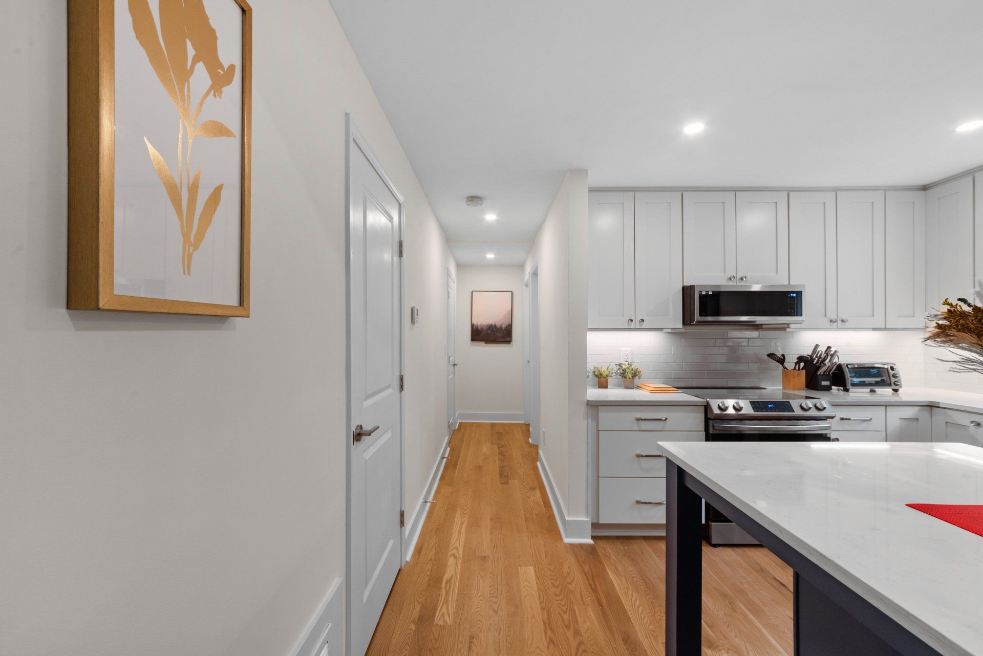 A kitchen with white cabinets and hardwood floors and a picture on the wall.