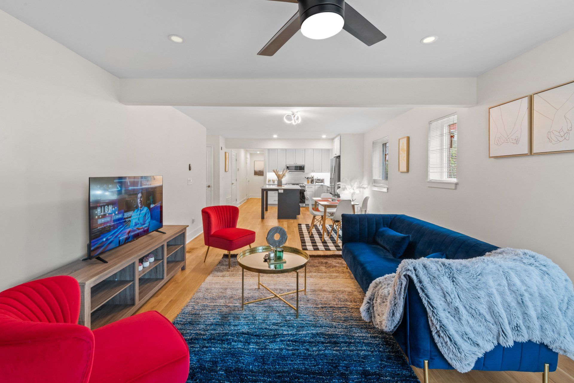 A living room with a blue couch , red chairs , a television and a ceiling fan.