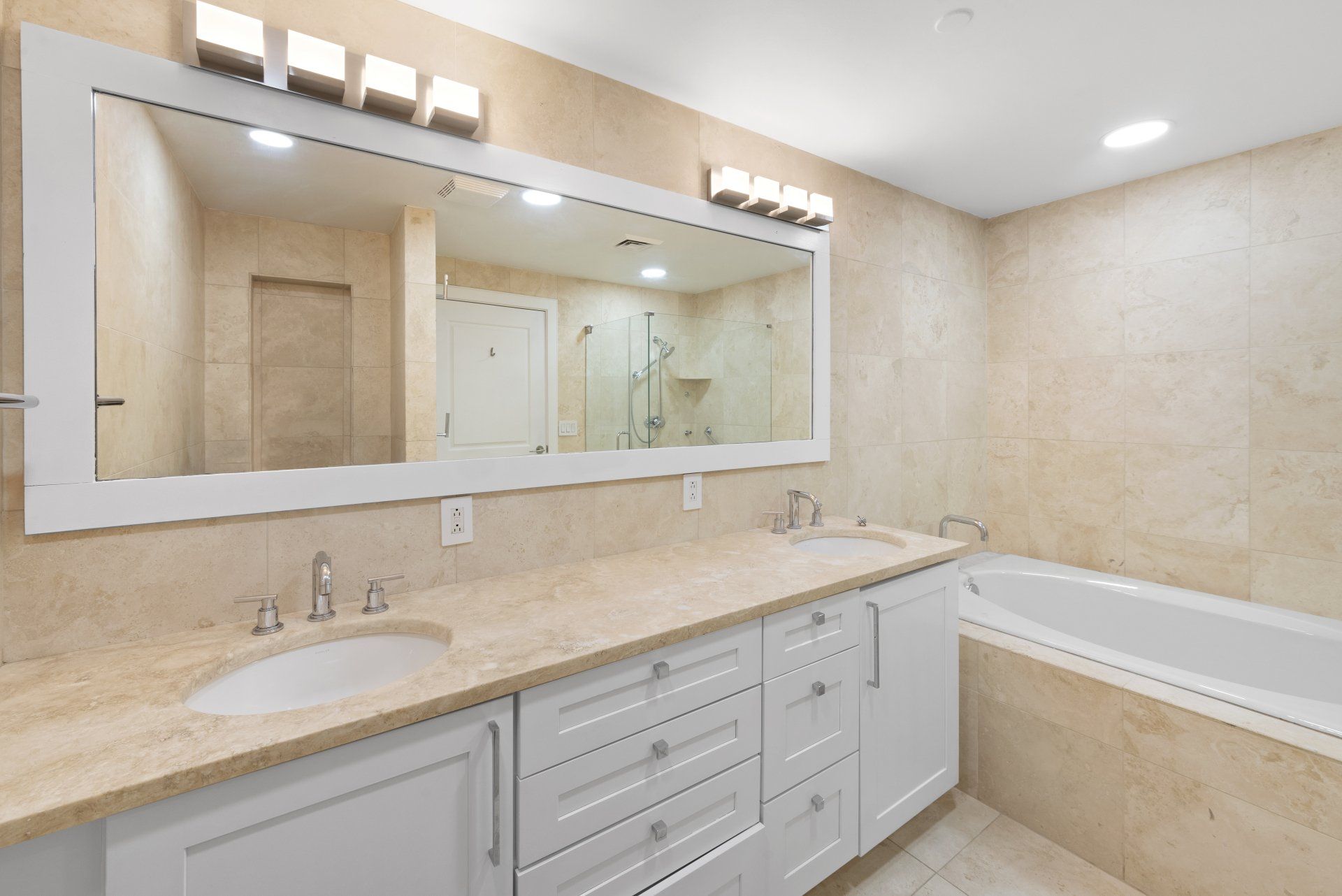 A bathroom with two sinks , a tub and a large mirror.