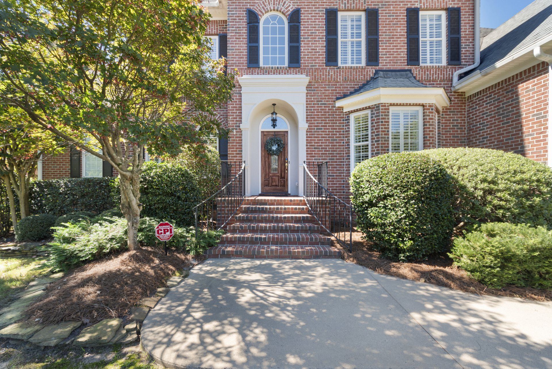A large brick house with black shutters and a large driveway.