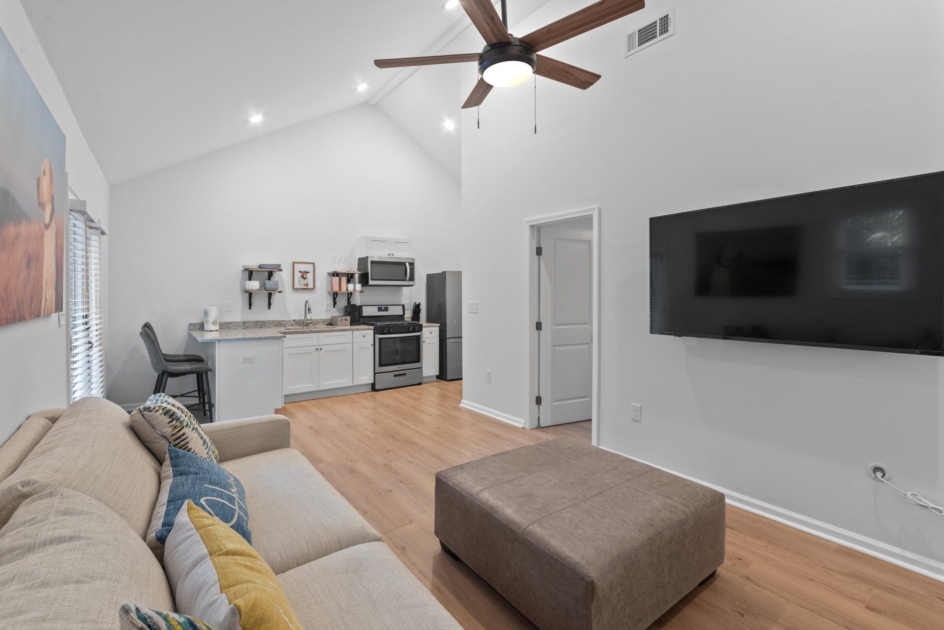 A living room with a couch , ottoman , television and ceiling fan.