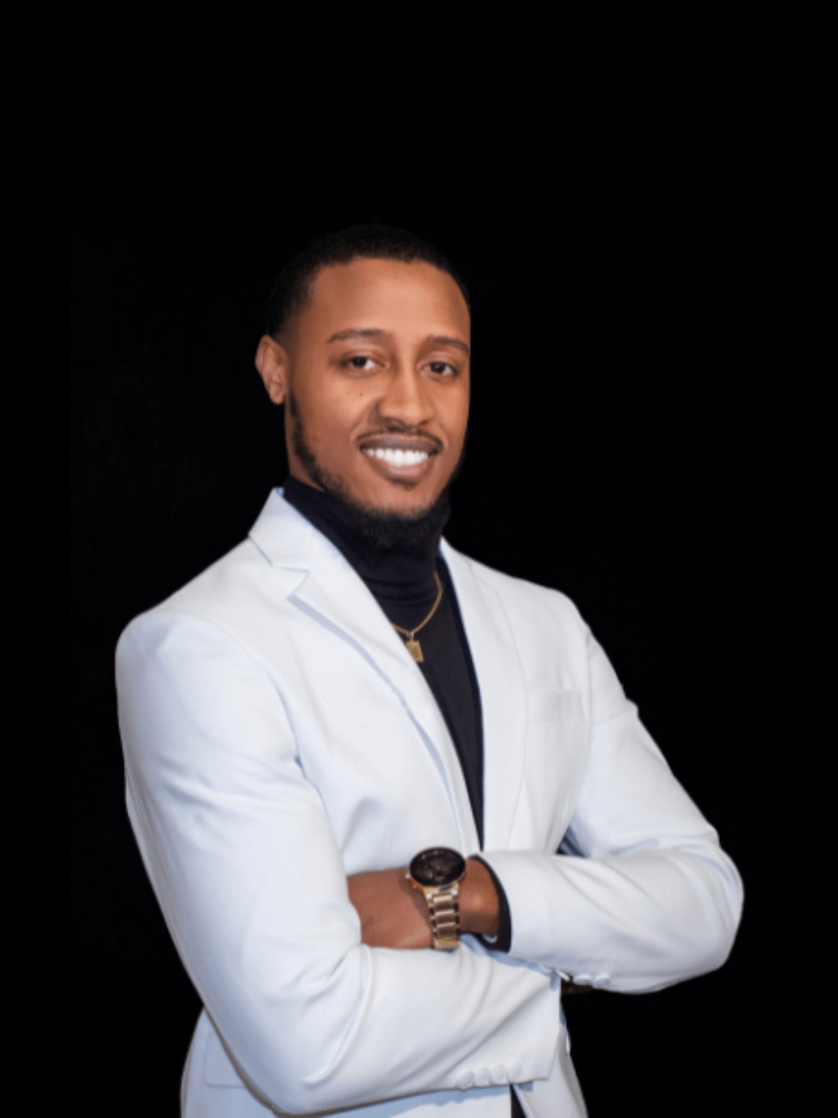 A man in a white suit and black turtleneck is standing with his arms crossed.