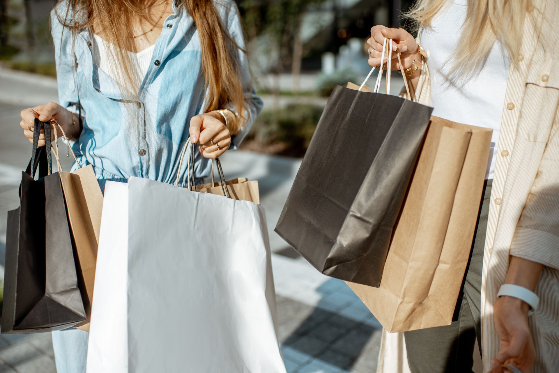 People carrying shopping bags on a sunny city street. Schedule your tour today to see why TwentyNine02 is a top destination for Apartments for Rent in Universal City, TX.