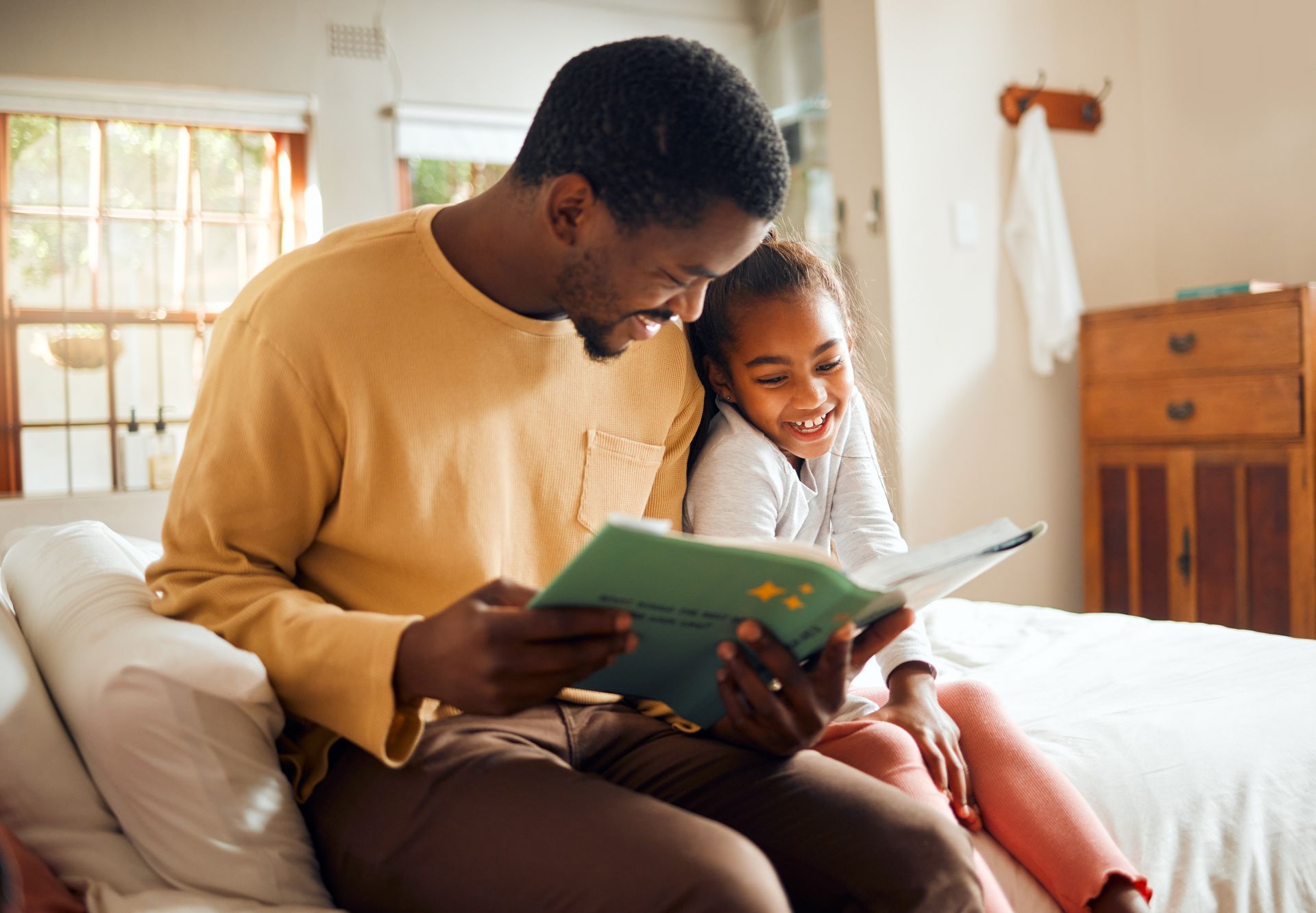 Adult reading a book with a child on a couch in a sunlit room. See what makes TwentyNine02 a top choice for Universal City, TX Rentals by scheduling your tour today.