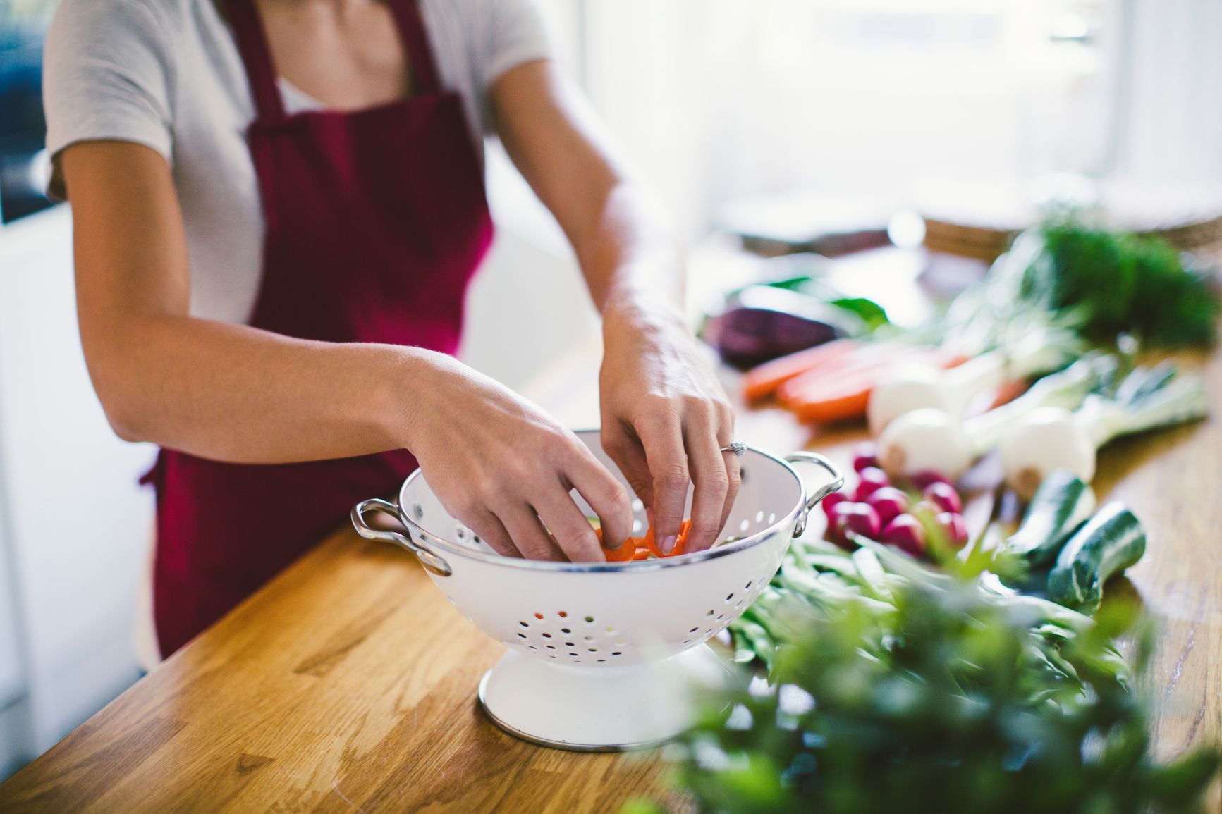 Person rinsing vegetables in a colander on a wooden kitchen counter. Take a tour of TwentyNine02 and discover modern Rentals in Universal City, TX designed for everyday living.