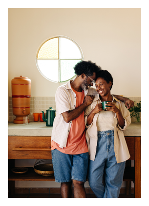 Two people smiling and looking at a phone together in a bright kitchen.